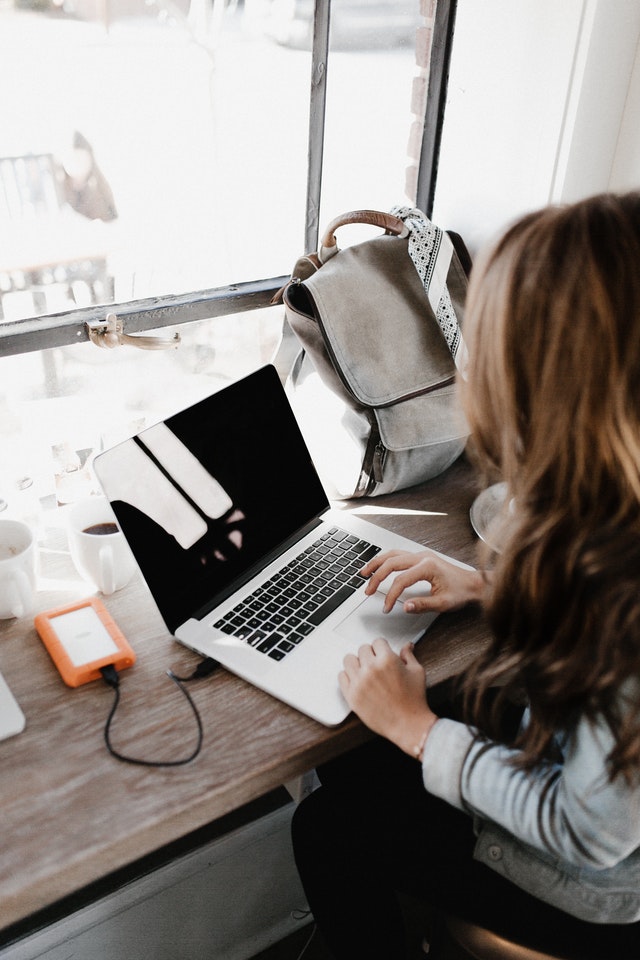 woman on the computer is typing out something while her phone charges in the port 