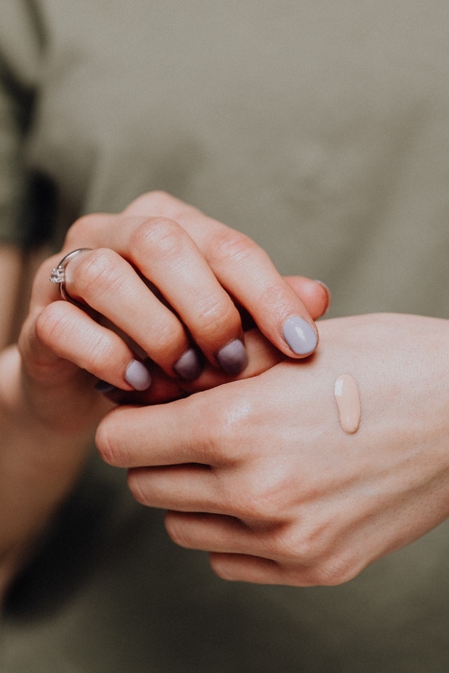 woman is wearing a ring and applying foundation to her hand 