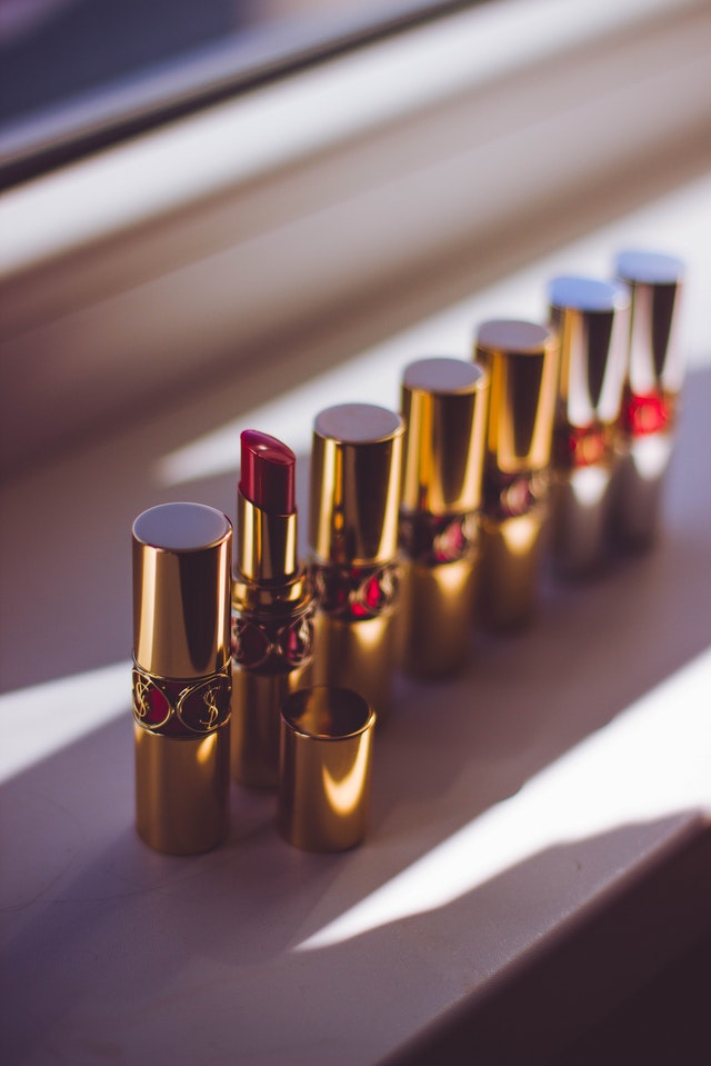 A bunch of YSL lipstick tubes are displayed neatly in a row with caps on. One lipstick tube has the cap off to expose a red lipstick underneath.